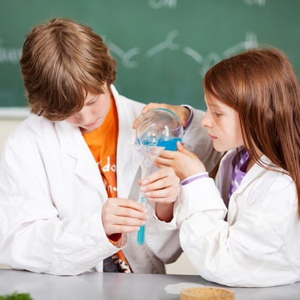 Young boy and girl in school learning chemistry working together as a team pouring liquids through a funnel into a test tube